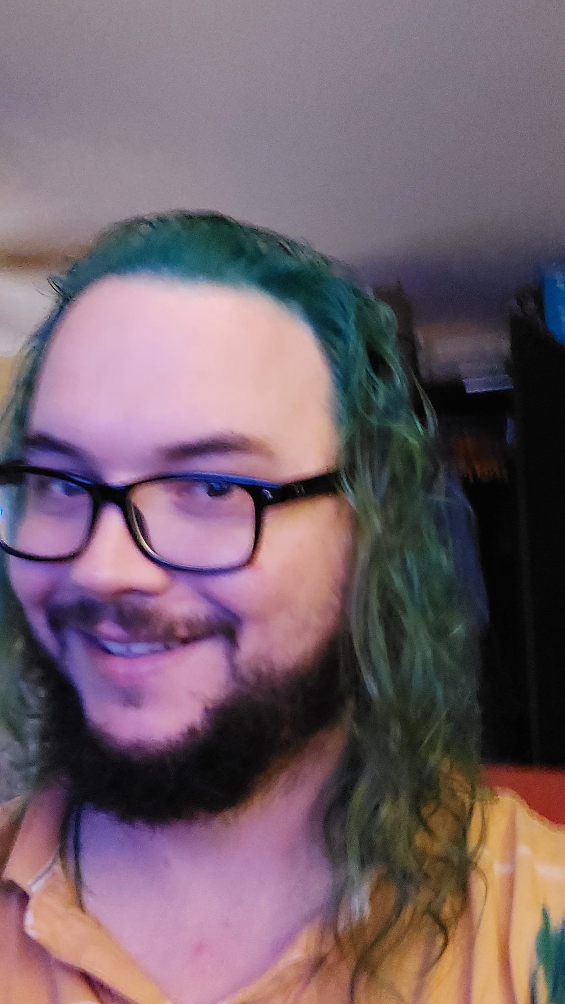 A man with long green hair sits in a computer chair